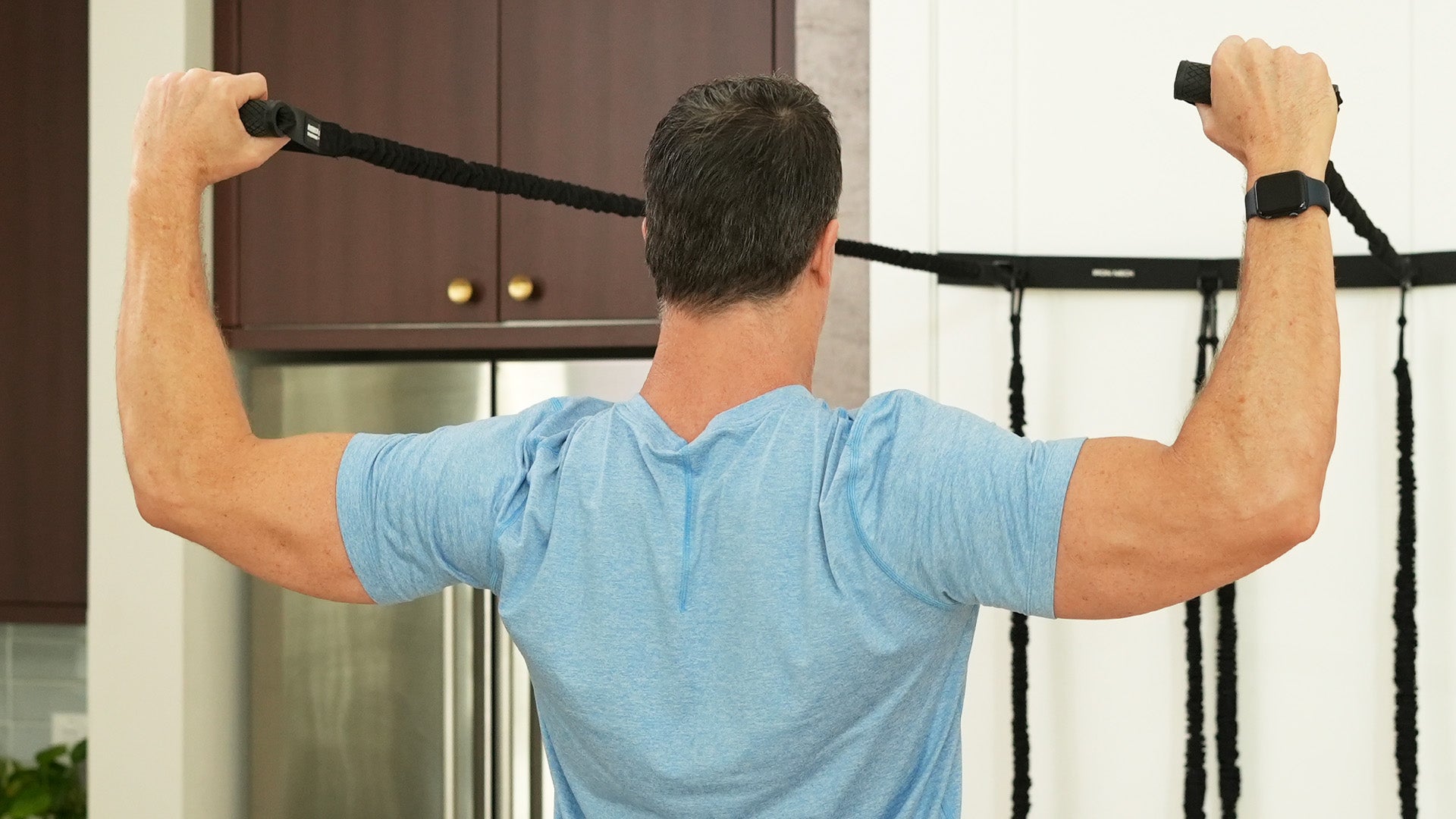 Man exercising using Iron Neck Shoulder bands in a home setting.